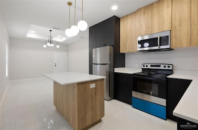 Kitchen featuring stainless steel appliances, modern cabinets, decorative light fixtures, a kitchen island, and a tray ceiling