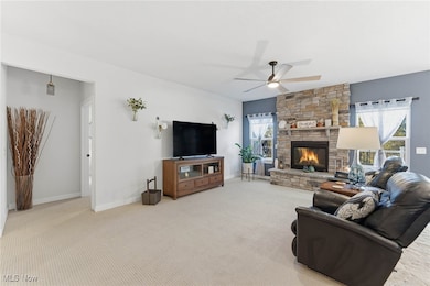Living area featuring carpet flooring, plenty of natural light, a stone fireplace, and a ceiling fan
