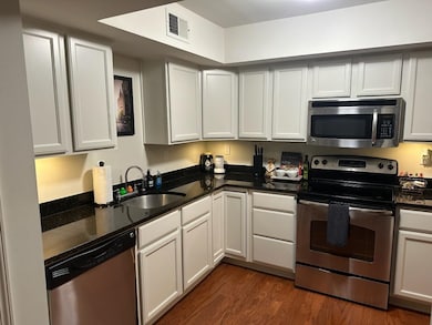 Kitchen featuring appliances with stainless steel finishes, dark wood-style flooring, and dark stone counters