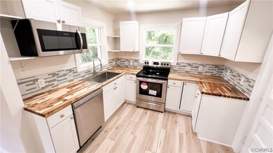 Kitchen with white cabinets, butcher block countertops, backsplash, and stainless steel appliances