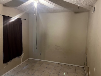 Empty room with a textured ceiling, light tile patterned flooring, and ceiling fan