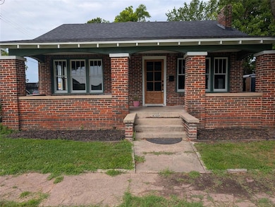 View of front of house with a chimney, brick siding, and roof with shingles