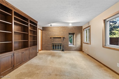 Living room featuring light colored carpet, a brick fireplace, rail lighting, brick wall, and a textured ceiling
