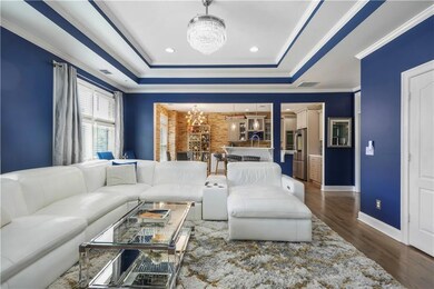 Living room with a chandelier, a tray ceiling, dark wood-style floors, and ornamental molding
