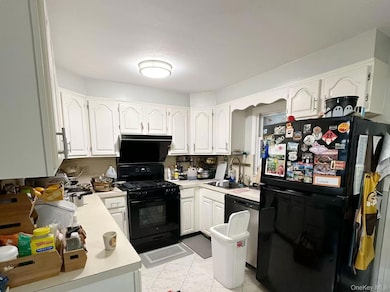 Kitchen with black appliances, light countertops, white cabinets, and light marble finish floors
