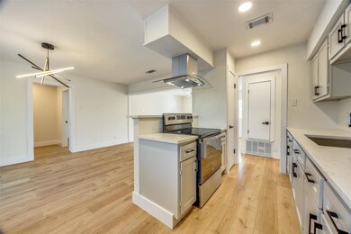Kitchen featuring stainless steel electric stove, sink, island range hood, a chandelier, and light hardwood / wood-style flooring