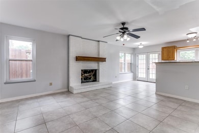 Living room with brick wall, a brick fireplace, ceiling fan, light tile floors, and french doors