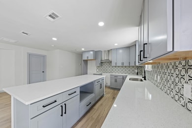 Kitchen with gray cabinetry, a sink, light wood-st