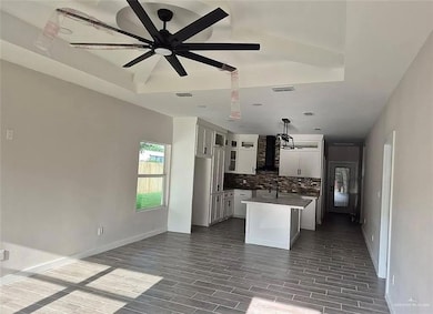 Kitchen with white cabinetry, a kitchen island with sink, wood tiled floors, decorative backsplash, and wall chimney range hood