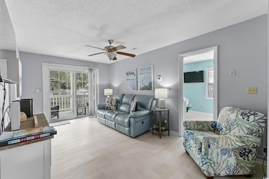 Living room featuring a ceiling fan, a textured ceiling, baseboards, and light wood finished floors