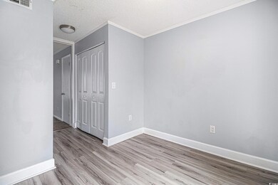 Empty room featuring light wood-type flooring, ornamental molding, baseboards, and a textured ceiling