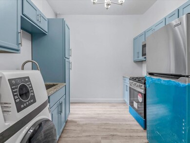 Kitchen with blue cabinetry, stainless steel appliances, stacked washer / dryer, light wood-type flooring, and baseboards