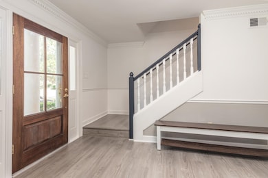 Entrance foyer with wood finished floors, healthy amount of natural light, stairs, and ornamental molding