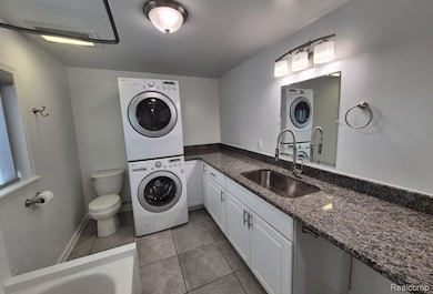 Full bath featuring stacked washer and clothes dryer, light tile patterned floors, vanity, and a garden tub