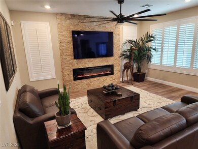 Living area featuring a stone fireplace, Luxury Vinyl floors, a ceiling fan and Shutters
