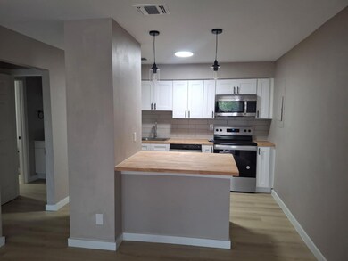 Kitchen with white cabinetry, stainless steel appliances, decorative backsplash, butcher block countertops, and pendant lighting