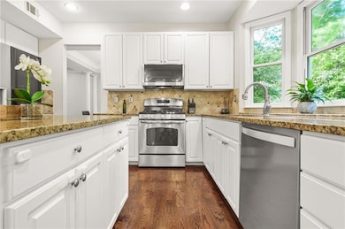 Kitchen featuring stainless steel appliances, white cabinetry, dark wood-style flooring, tasteful backsplash, and recessed lighting