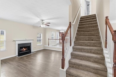 Staircase featuring wood finished floors, a chandelier, a lit fireplace, and a ceiling fan