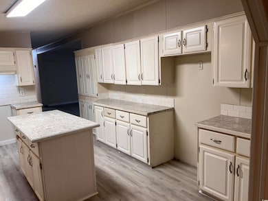 Kitchen featuring decorative backsplash, light wood-type flooring, white cabinets, a center island, and under cabinet range hood