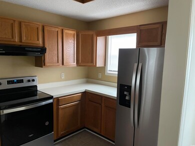 Kitchen with appliances with stainless steel finishes, range hood, light countertops, dark tile patterned flooring, and a textured ceiling