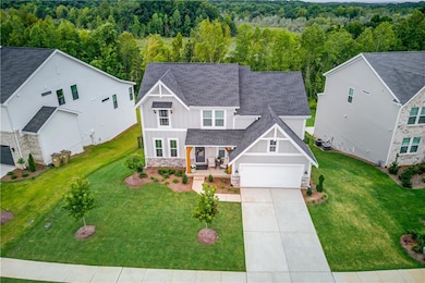 View of front facade featuring board and batten siding, roof with shingles, covered porch, concrete driveway, and stone siding. Home has private green space in both the front and back.