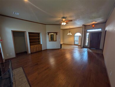 Unfurnished living room featuring ornamental molding, dark wood-style flooring, a chandelier, a ceiling fan, and built in shelves