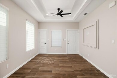 Living room featuring a raised ceiling, dark wood-style floors, and ceiling fan