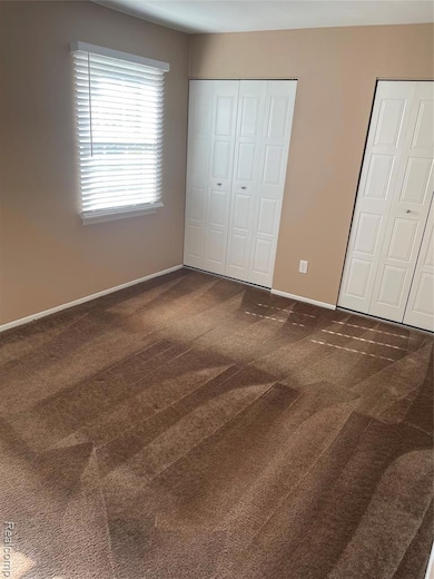 Unfurnished bedroom with dark colored carpet and two closets