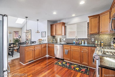 Kitchen with a peninsula, a skylight, stainless steel appliances, brown cabinets, and pendant lighting