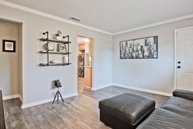 Living room with estacked washer and dryer, crown molding, and wood finished floors