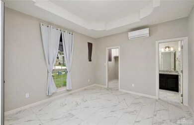 Unfurnished bedroom with ensuite bathroom, a tray ceiling, a wall unit AC, a spacious closet, and light tile floors