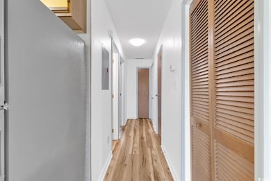 Hall featuring a heating unit, light wood finished floors, baseboards, and electric panel