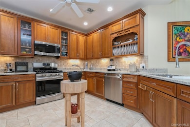 Kitchen featuring stainless steel appliances, brown cabinetry, light stone countertops, tasteful backsplash, and recessed lighting
