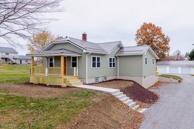 View of front of home featuring a chimney, a metal roof, covered porch, and an outdoor structure