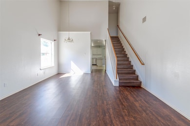 Unfurnished living room featuring a high ceiling, dark wood-type flooring, a chandelier, and stairs