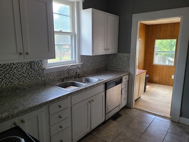 Kitchen with backsplash, white cabinetry, dishwashing machine, light tile patterned floors, and wood walls