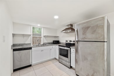 The kitchen is outfitted with stainless steel appliances, white cabinetry, and custom shelving—offering a modern, low-maintenance design.