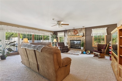 Carpeted living room with a stone fireplace and ceiling fan