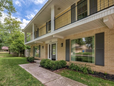 Entrance to property featuring a balcony, brick siding, and a yard