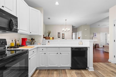 Kitchen with black appliances, white cabinets, decorative light fixtures, kitchen peninsula, and light wood-type flooring