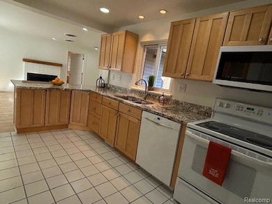 Kitchen featuring white appliances, light tile patterned flooring, dark stone counters, recessed lighting, and a brick fireplace