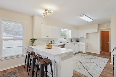 Kitchen featuring kitchen peninsula, a kitchen bar, light wood-type flooring, white cabinetry, and tasteful backsplash