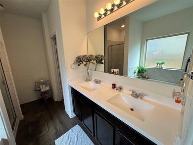 Bathroom with dark wood-style flooring, double vanity, and a shower stall