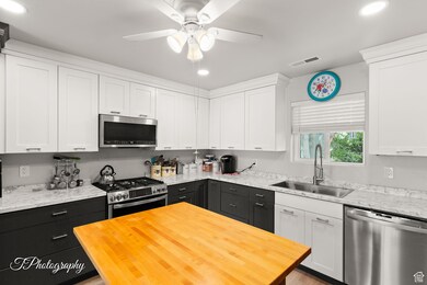 Kitchen featuring stainless steel appliances, white cabinets, recessed lighting, light stone counters, and a ceiling fan