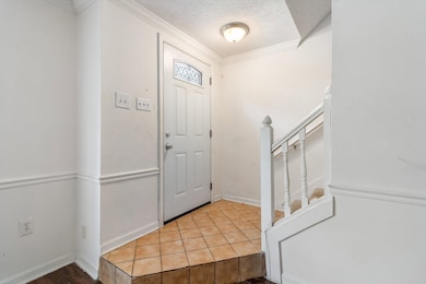 Entryway with a textured ceiling, tile patterned floors, stairway, and ornamental molding
