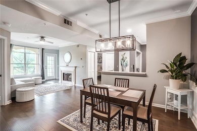 Dining room featuring ornamental molding, dark wood-type flooring, a ceiling fan, baseboards, and a glass covered fireplace