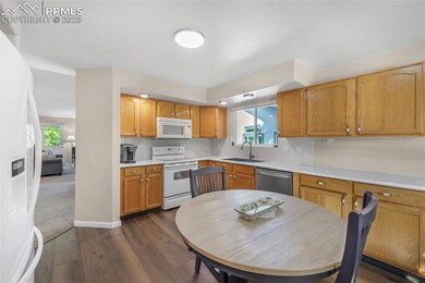 Kitchen with white appliances, a sink, light countertops, dark wood-style floors, and backsplash