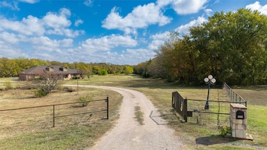 View of dirt / gravel driveway featuring a view of countryside, a wooded view, and a gated entry