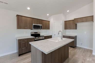 Kitchen featuring appliances with stainless steel finishes, light countertops, a kitchen island with sink, light wood-type flooring, and vaulted ceiling