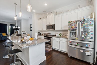 Kitchen featuring stainless steel appliances, crown molding, dark wood-style flooring, white cabinets, and light stone countertops